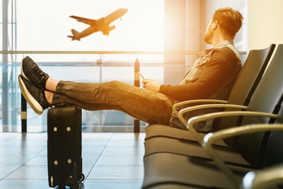 一个男人坐在椅子上，脚放在行李上，看着飞机